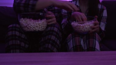 Pijamalı evli bir çift televizyonun önünde oturmuş patlamış mısır yiyor. Covid-19 salgını sırasında ev karantinası.