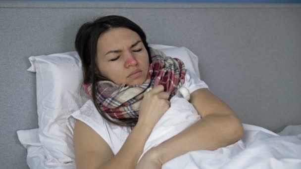 Sjuk ung kvinna ligger i sängen och mäter temperaturen. Hon har hosta, frossa, rinnande näsa. Influensa-, förkylnings- eller coronavirussymtom. — Stockvideo