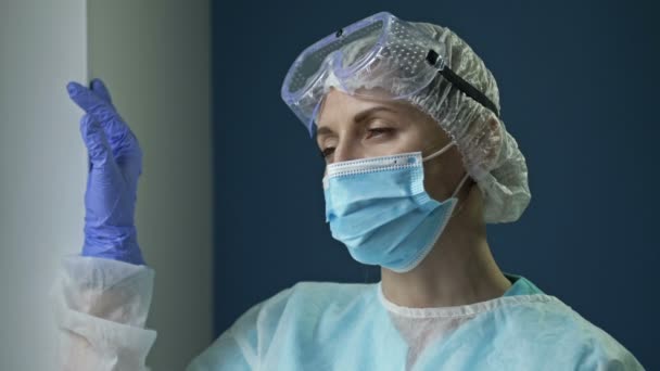 Ritratto di medico o infermiere donna stanca in uniforme protettiva. La donna guarda in lontananza con attenzione. La dura vita quotidiana degli operatori sanitari durante la pandemia di Covid-19. — Video Stock