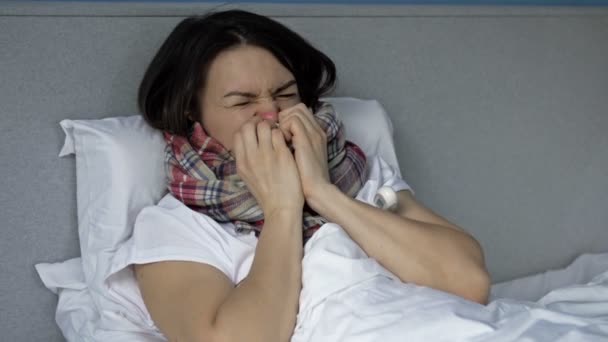 Beteg fiatal nő fekszik az ágyban, és méri a hőmérsékletet. Köhögés, hidegrázás, orrfolyás. Influenza, megfázás vagy koronavírus tünetei. — Stock videók