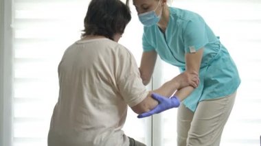 Doktor ya da hemşire yaşlı bir kadının ayağa kalkmasına yardım ediyor. Yaralanma, ameliyat ya da felç sonrası iyileşme.