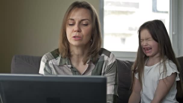 La mujer está tratando de trabajar en casa. La aburrida hija preescolar quiere atraer la atención de sus madres chillando y llorando. Las dificultades de la cuarentena domiciliaria. — Vídeos de Stock