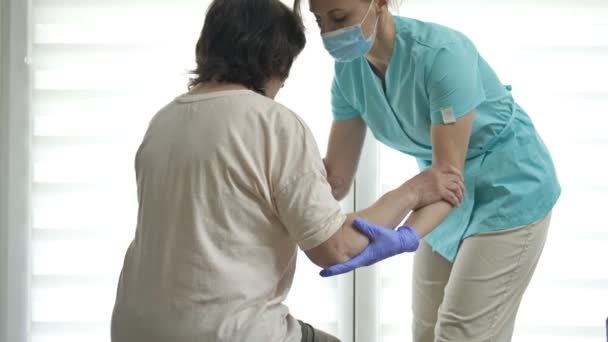 Doktor ya da hemşire yaşlı bir kadının ayağa kalkmasına yardım ediyor. Yaralanma, ameliyat ya da felç sonrası iyileşme. — Stok video