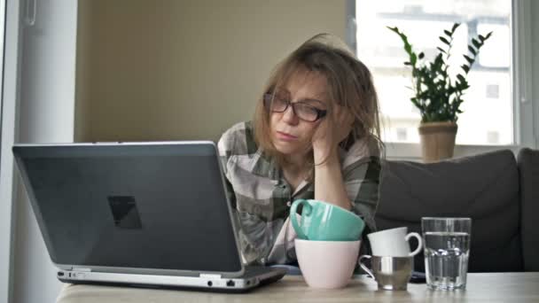 自宅でノートパソコンを操作する非常に疲れているビジネス女性。テーブルの上にはお茶とコーヒーの空のカップがいくつかあります。女は疲労で眠りにつく。働き過ぎの概念. — ストック動画