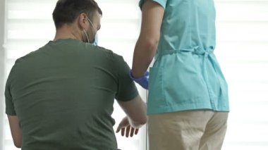 Doktor ya da hemşire bir hastanın ayağa kalkmasına yardım ediyor. Yaralanma, ameliyat ya da felç sonrası iyileşme. Covid-19 salgını sırasında tedavi.