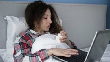 Hasta kadın dizüstü bilgisayar ve akıllı telefonla kendini izole ederek yatakta yatıyor. Coronavirus covid-19 karantinasında çalışıyor. Uzak çalışma.