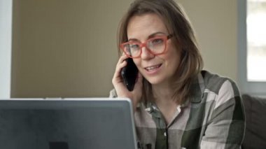 İş kadınının keyfi yerinde. Güzel orta yaşlı bir kadın dizüstü bilgisayarının önünde oturmuş cep telefonuyla biriyle konuşurken eğleniyor..