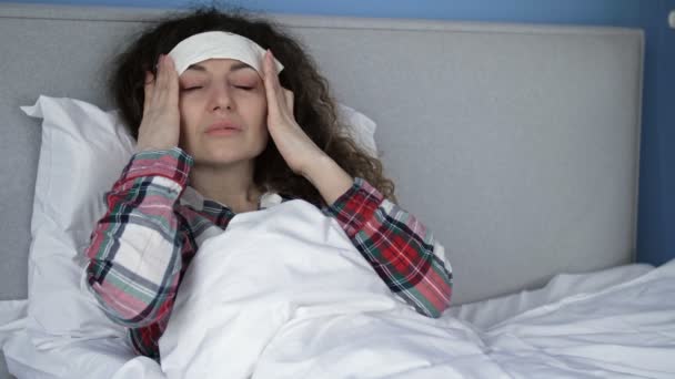 Baş ağrısından muzdarip hasta bir kadının portresi ve alnında soğuk ıslak bir kompres taşıyor. Migren, akşamdan kalma ya da yüksek ateş. — Stok video