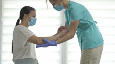 Doktor ya da hemşire bir kadın hastaya ayağa kalkması için yardım ediyor. Yaralanma, ameliyat ya da felç sonrası iyileşme. Yüz kalkanları. Covid-19 salgını sırasında tedavi.