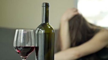 Bir şişe şarap ve bir bardak yakın çekim. Gözyaşları içindeki kadın yalnız başına şarap içiyor. Kadın alkolizmi - sosyal sorun.