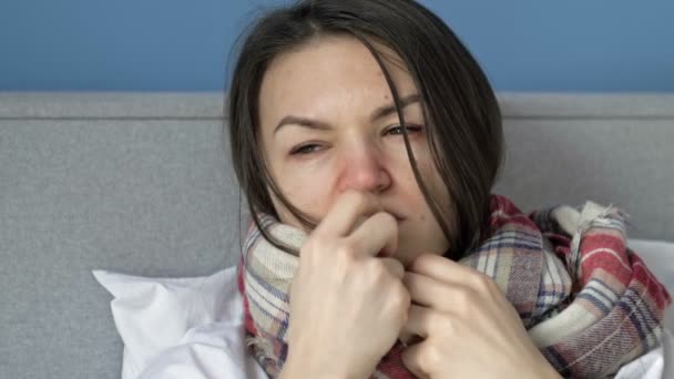 Молодая женщина лежит в постели завернутая в шарф. У нее симптомы гриппа, простуды или коронавируса. — стоковое видео