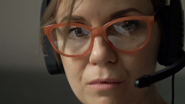 戴着耳机和话筒的漂亮而严肃的女人的特写，戴着能反射电脑屏幕的眼镜. — 图库视频影像