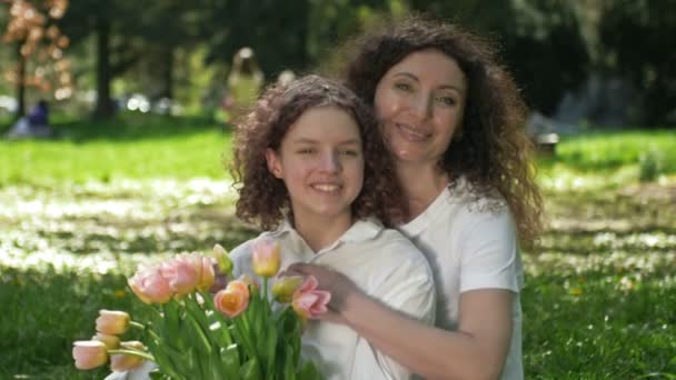 Portret van een vrouw die haar tienerdochter omhelst met een boeket tulpen. Tegen de achtergrond van de lente natuur. Moederdag. — Stockvideo