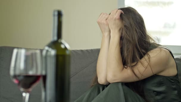 Közelkép egy üveg borról és egy pohárról. A könnyes nő egyedül iszik bort. Női alkoholizmus - társadalmi probléma. — Stock videók