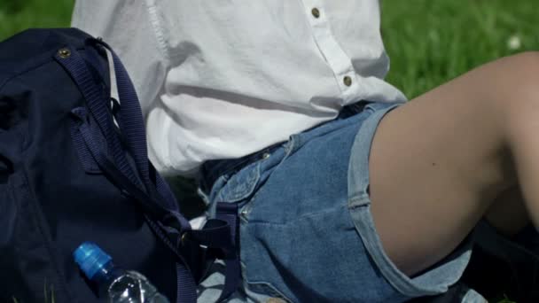 Счастливая девочка-подросток сидит на траве, наслаждается солнечным днем, слушает музыку в наушниках и поет. — стоковое видео