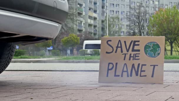 Salve o cartaz do PLANET ao lado do tubo de escape de um carro. — Vídeo de Stock