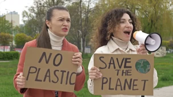 Due donne sono in piedi con manifesti RISPARMIA IL PIANETA e NESSUN PLASTICO. Uno di loro usa un megafono per chiedere la protezione dell'ambiente. Contributo fattibile alla lotta contro la globalizzazione — Video Stock