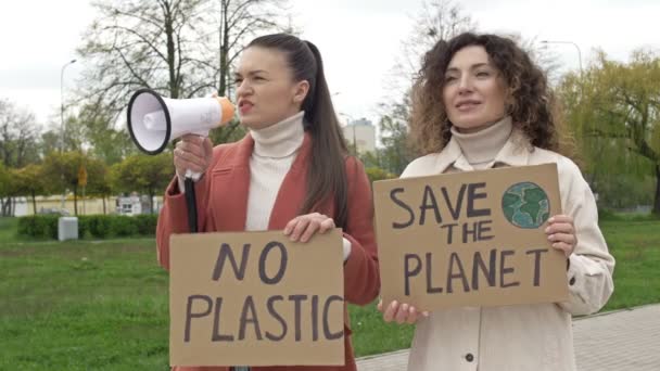 Duas mulheres estão de pé com cartazes SALVAR O PLANETA e NÃO PLÁSTICO. Um deles usa um megafone para pedir a proteção do meio ambiente. Contribuição viável para a luta contra a globalização — Vídeo de Stock