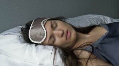 Yorgun bir kadın yatağa düşer, uyku maskesi takar ve anında uykuya dalar..
