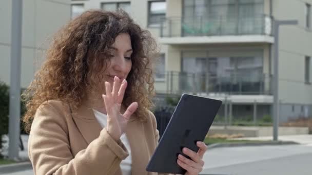 Mujer de pelo rizado de mediana edad pasea por una calle desierta de la ciudad. Se comunica con alguien a través de una tableta. — Vídeos de Stock