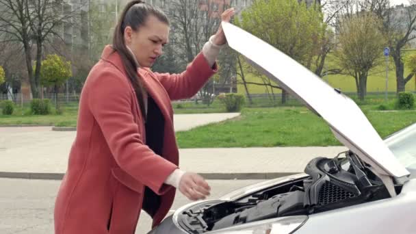 Wanita muda yang menggunakan smartphone, meminta bantuan atau truk derek ketika berdiri di dekat mobilnya dengan kap terbuka di pinggir jalan. — Stok Video