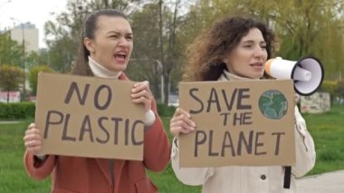 İki kadın ellerinde posterlerle durup gezegeni kurtarıyorlar ve plastikleri yok. Bir tanesi, çevrenin korunması için megafon kullanıyor. Küresel mücadeleye makul bir katkı