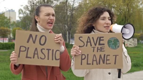 Két nő áll a plakátokkal, a PLANET-et és a NO PLASTIC-ot mentették meg. Egyikük egy hangosbeszélőt használ a környezet védelmére. A globális küzdelem megvalósítható hozzájárulása — Stock videók