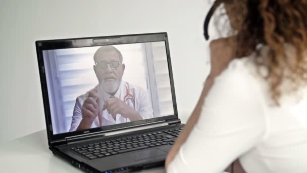 Telemedicina. Uma mulher sentada na frente de um laptop em seu apartamento consulta seu médico através da Internet. Troca de experiências online entre dois médicos. — Vídeo de Stock