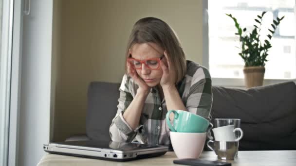 La mujer de negocios trabajando desde casa está muy cansada. Hay varias tazas vacías de té y café en la mesa. Concepto de trabajo excesivo. — Vídeos de Stock