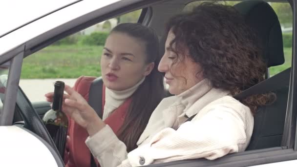 Two girlfriends drink wine from a bottle while sitting in the car. Drunk driving. — Stock Video