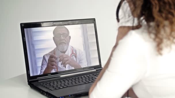 Telemedicina. Una mujer sentada frente a un portátil en su apartamento consulta con su médico a través de Internet. Intercambio de experiencias en línea entre dos médicos. — Vídeo de stock