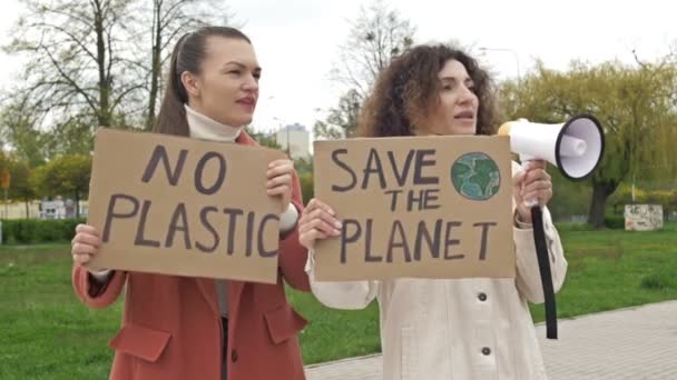 Dwie kobiety stoją z plakatami "Uratuj PLANETA" i "NIE PLASTYCZNIE". Jeden z nich używa megafonu, aby wezwać do ochrony środowiska. Faktyczny wkład w walkę z globalnym — Wideo stockowe