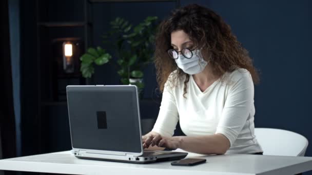Büroarbeit während der Coronavirus-Epidemie. Geschäftsfrau mit medizinischer Maske schaut in eine Webcam und spricht mit jemandem. — Stockvideo