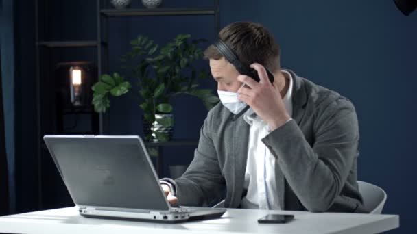 Lavora durante l'epidemia di coronavirus. Uomo d'affari stanco di mezza età con sollievo rimuove la maschera medica, cuffie e chiude il computer portatile alla fine della giornata lavorativa. — Video Stock