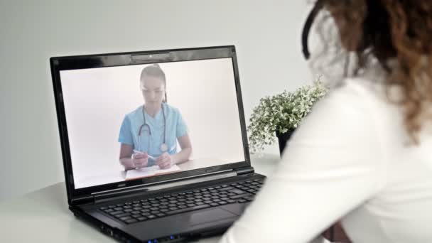 Telemedicina. La mujer sentada frente a un portátil en su apartamento consulta con su médico a través de Internet. Intercambio de experiencias en línea entre dos médicos. — Vídeos de Stock