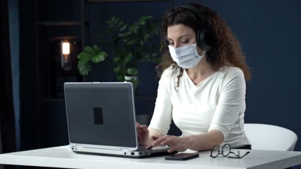 Praca biurowa podczas epidemii koronawirusów. Bizneswoman w masce medycznej patrzy w kamerkę internetową laptopa i rozmawia z kimś. — Wideo stockowe