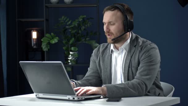Porträt eines Mannes mittleren Alters, der an einem Laptop arbeitet. Er ist fokussiert, überlegt und spricht mit dem Kunden. Distanzierte Arbeit. — Stockvideo