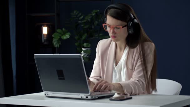 Femme d'affaires sérieuse concentrée avec écouteurs utilisant un ordinateur portable pendant l'appel vidéo. Emploi à distance pendant le coronavirus. Jeune femme en fonction. — Video