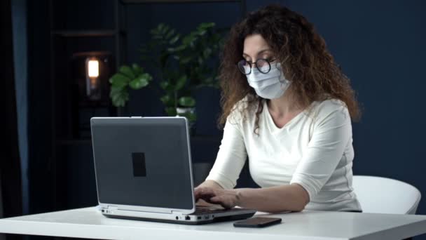 Werk tijdens de coronavirusepidemie. Moe zakenvrouw van middelbare leeftijd met verlichting verwijdert zijn medische masker, koptelefoon en sluit de laptop aan het einde van de werkdag. — Stockvideo