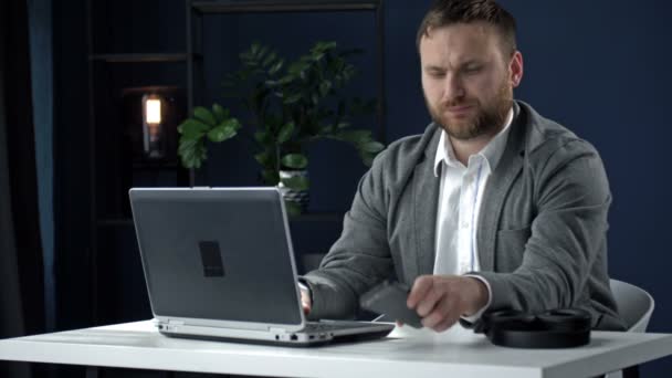 Серйозний бізнесмен використовує ноутбук і сучасний смартфон для офісної роботи . — стокове відео