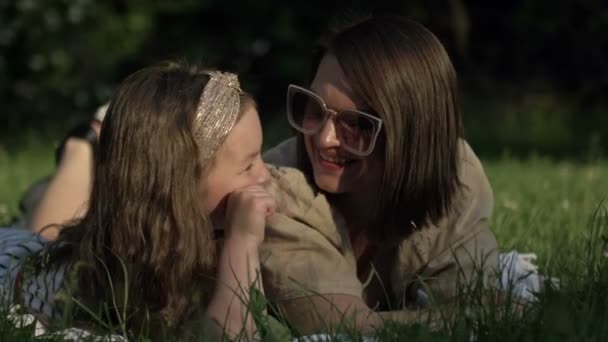 Retrato de verão de mãe e filha pré-escolar deitada na grama no parque. Ambos olham para a distância e sorriem. Dia das Mães. — Vídeo de Stock