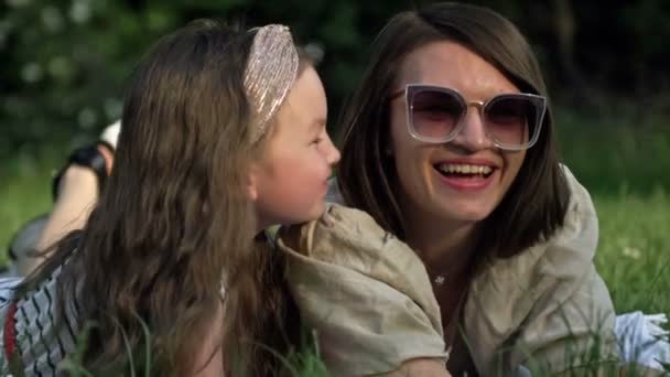 Zomer portret van moeder en kleuter dochter liggend op het gras in het park. De baby kust zachtjes haar moeder. Moederdag. — Stockvideo