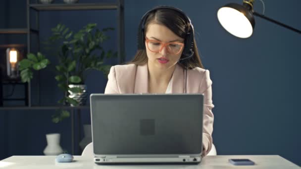 Ritratto di una giovane donna con un auricolare che lavora in un computer portatile. Operatore di call center educato. Donna d'affari comunica con un sorriso con i partner commerciali. — Video Stock