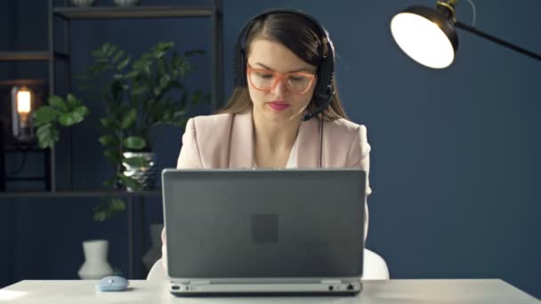 헤드폰을 쓴 젊은 여성의 초상화가 노트북에서 일하고 있습니다. 폴이 트 콜 센터 오퍼레이터. 사업을 하는 여자는 사업 동료들 과 미소를 지으며 의사소통을 한다. — 비디오