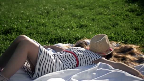 Niño acostado en una manta de picnic en el parque de verano. Chica extendió sus brazos hacia los lados, su cara cubierta con un sombrero de paja. — Vídeos de Stock