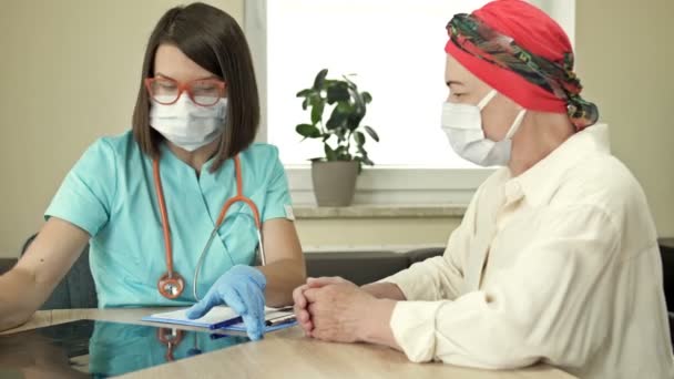 Une femme âgée chez l'oncologue, consultation sur les résultats de la chimiothérapie. Médecin et patient portant des masques de protection, Covid-19 pandémie. — Video
