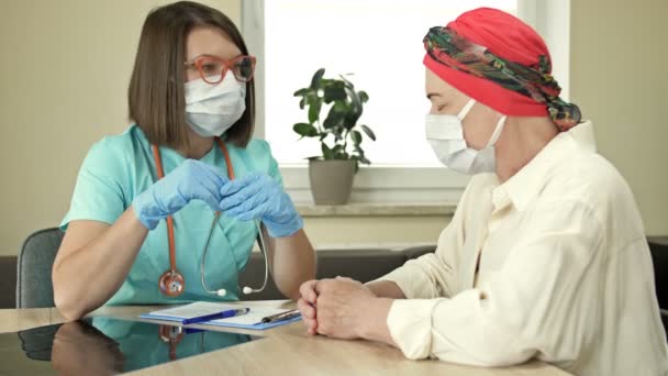 Una mujer mayor en el oncólogo, consulta sobre los resultados de la quimioterapia. Médico y paciente con máscaras protectoras, pandemia de Covid-19. — Vídeos de Stock