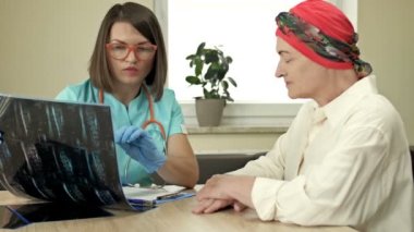 Onkolojistteki yaşlı bir kadın, kemoterapi sonuçları için danışmanlık, iyi haber. Gülümseyen genç bir bayan doktor hastayı sakinleştirir ve ona destek olur..