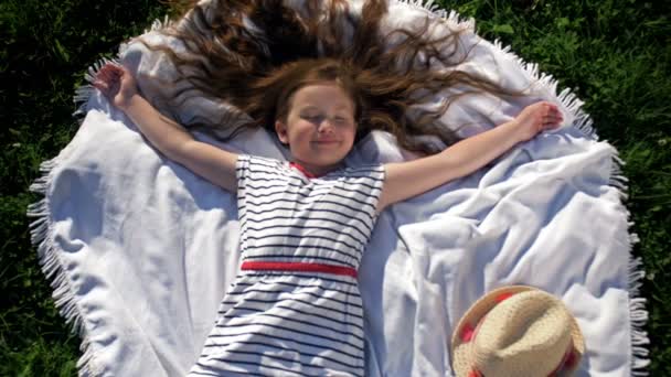 Criança deitada em cobertor fazendo piquenique no parque de verão. Menina abriu os braços para os lados. — Vídeo de Stock