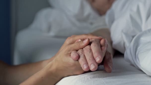 Fürsorgliche junge Hand, die die Hand eines alten und kranken geliebten Menschen hält. Liebe, Mitgefühl und familiäre Unterstützung. Nahaufnahme. — Stockvideo